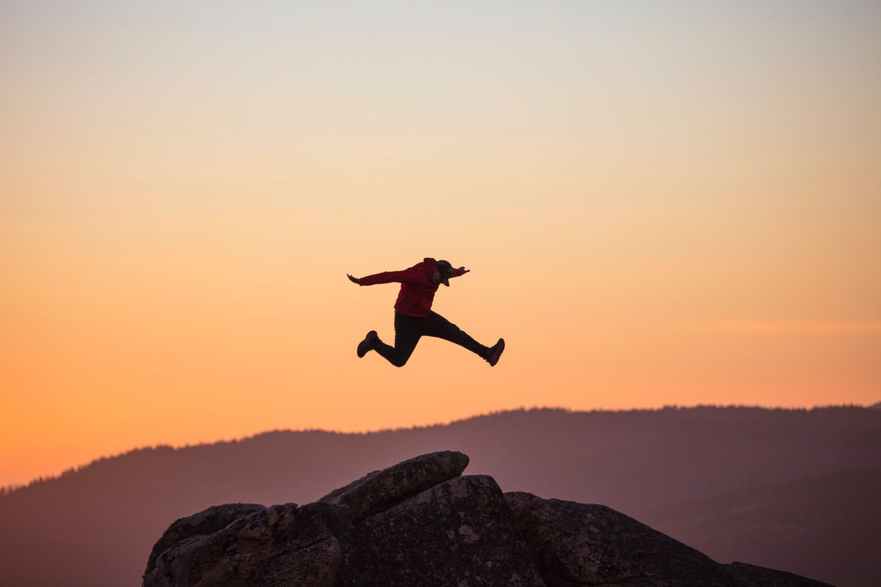 Silhouette of a man jumping on rocks at sunrise, showcasing motion and adventure.